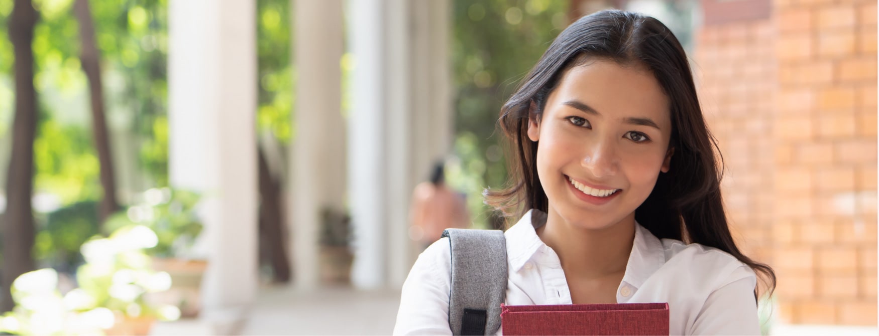 海外留学生の女性がリュックを背負って赤い本を持って微笑んでいる写真